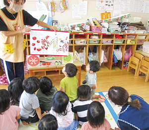 先生が持った野菜についての話を聞き、勉強する園児たちの写真