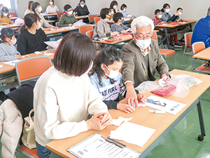 お母さんと小学生と高齢の男性が一緒に正月飾りを作っている写真