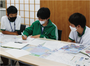 白根第一中学校２年生の男子生徒３人が相談しながら原稿書きをしている写真