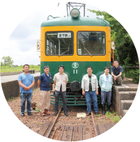 かぼちゃ電車保存会のメンバーがかぼちゃ電車の前に並んでいる写真