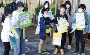 大鷲小学校4年生が西区「いっぺこーと」出入口で並び、チラシ配布をしている写真