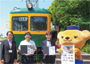 かぼちゃ電車の前で、三条井栗郵便局長とかぼちゃ電車保存会会長と新潟交通（株）総務課長と郵便局のキャラクターがフレーム切手を持ち立っている写真