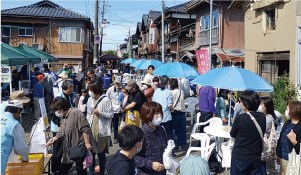 昨年の「味わい市場」の様子。小路いっぱいに出店と往来する人たち、水色のパラソル付の休憩テーブルがいくつか並ぶ左エ門小路の写真