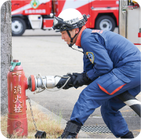 紺色のユニホームにヘルメットを着用した隊員が真剣な表情で、消火栓にホースを繋いでいる写真