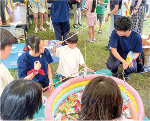 家庭用ビニールプールに入っているお菓子を魚に見立て、お菓子釣りをしている男の子を「大鷲夜まつりもりあげ隊」が見守っている写真